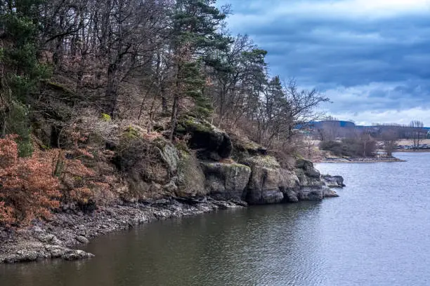 Rocky bank and trees along a river or lake with reflection on the water on a cloudy overcast day