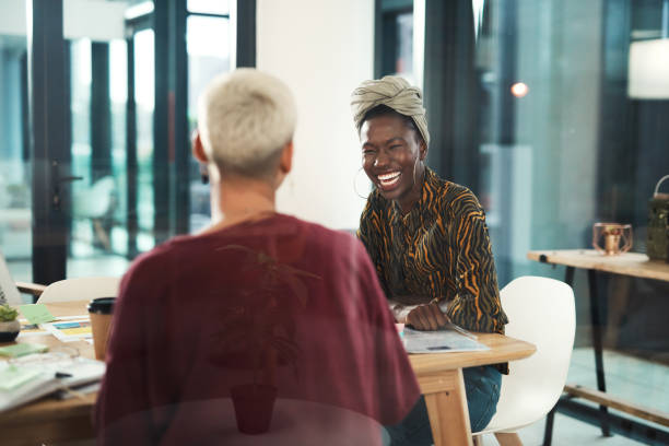 Sharing ideas is vital to success Cropped shot of an attractive young businesswoman sitting and laughing with her female colleague in the office professional people laughing stock pictures, royalty-free photos & images