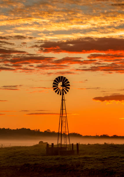 風車は鮮やかな日の出の空と農地に立っています - scenics landscape windmill sunrise ストックフォトと画像