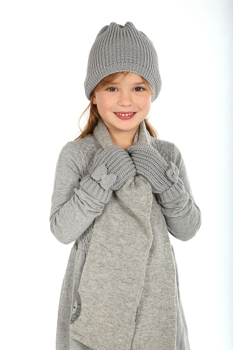 Cute girl with grey gloves, scarf and cap smiles into the camera