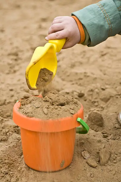 child filling plastic children bucket with sand