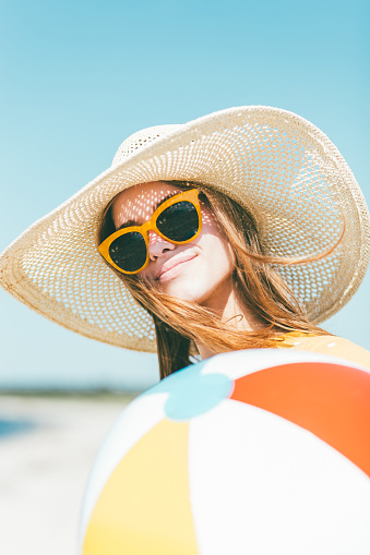 Close up portrait of young woman on the beach. Wearing a sun hat and holding beach ball in her hands.