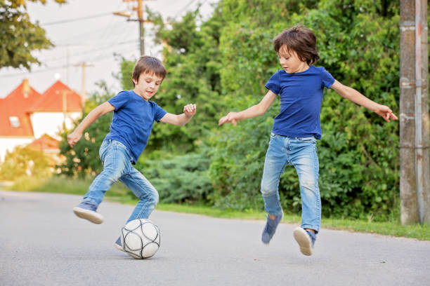 two cute little kids, playing football together, summertime. children playing soccer - footpath small green white imagens e fotografias de stock