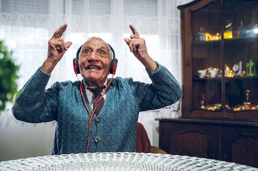 Senior, happy, man listening to the music, with headphones on. Making happy gestures. Home interior.