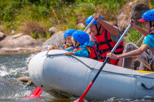 rafting-ausflug. eine fröhliche gruppe von männern und frauen steigt auf einem großen schlauchboot auf dem fluss hinab. im boot sitzt ein kind. - sports team sport rowing teamwork rafting stock-fotos und bilder