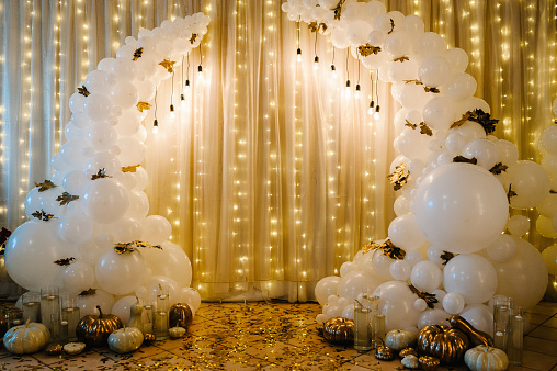 Decorated arch for wedding ceremony. White balloons, candles, autumn leaves and small pumpkins. Autumn location and Halloween decor.