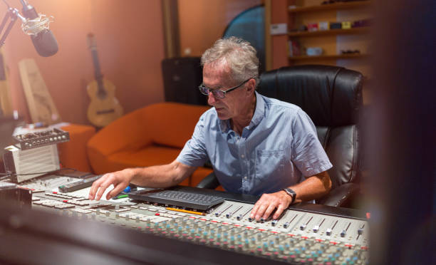 istock Male middle aged recording engineer in a recording studio sitting at a multi channel console 1170668103