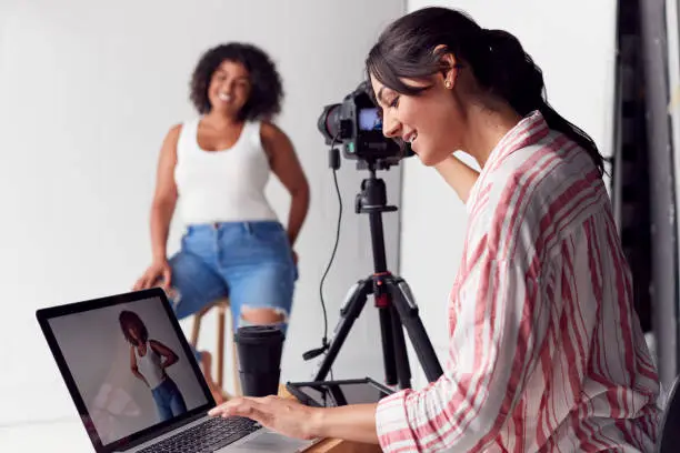 Photo of Female Photographer In Digital Studio Shooting Images On Camera Tethered To Laptop Computer
