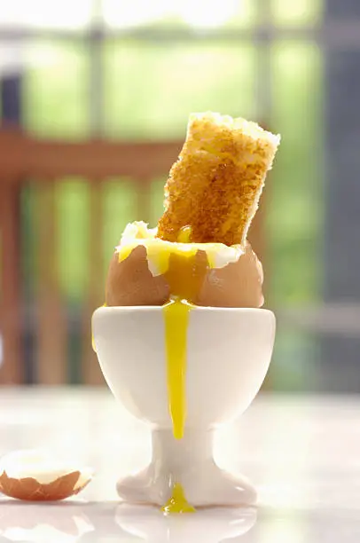 Soft boiled egg in egg cup with a piece of toast dipping in it (soldier).  Very Shallow DOF, focus on crack. 