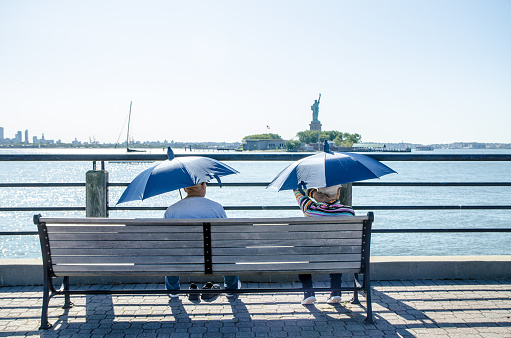 Mature man and woman looking at Statue of Liberty while sitting on a bench in the Liberty State Park in Jersey city during summer day