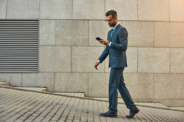istock Business message. Side view of handsome businessman in formal wear using smart phone while walking outdoors 1170677397