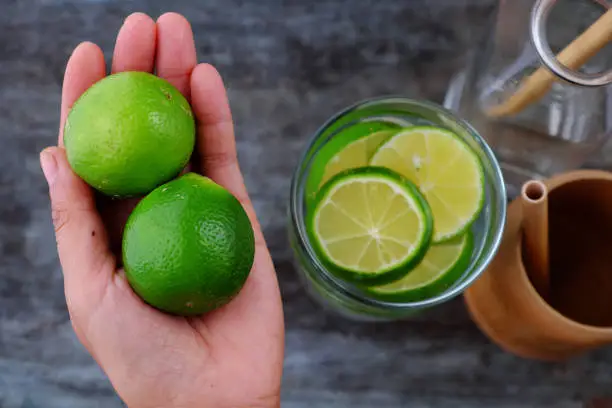 Close up woman hand hold lemons and lime slices for detox water on gray wooden background, a drinking water for healthy diet and skin care