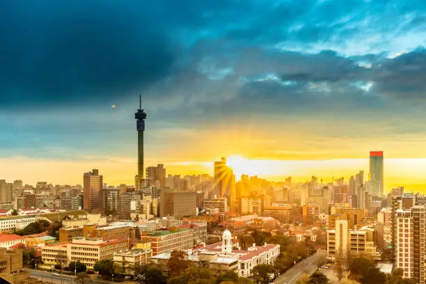 Johannesburg sunrise with a sunflare and dramatic sky, cityscape. Johannesburg is one of the forty largest metropolitan cities in the world, and the world's largest city that is not situated on a river, lakeside, or coastline. It is also the source of a large-scale gold and diamond trade, due being situated in the mineral-rich Gauteng province.