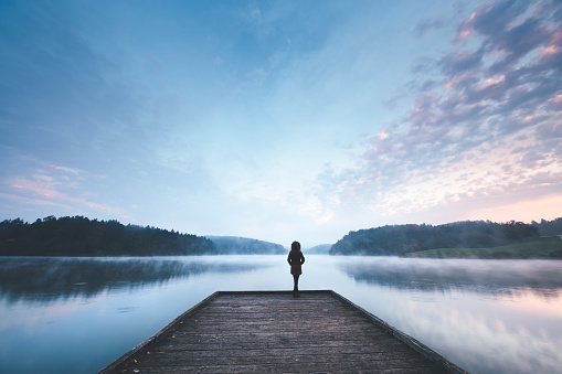 Woman standing on the jetty and watching colorful sunrise.