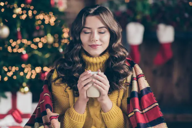 Close up photo of cheerful fun nice positive cute charming girl sensing nice, smell of drink wearing yellow pullover sitting in plaid enjoying her carefree leisure with cup of tea