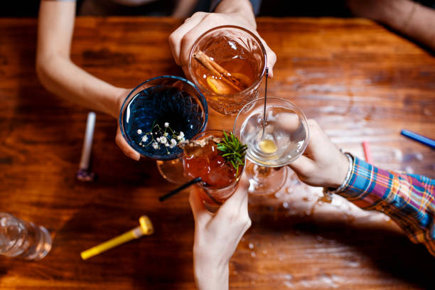 amigos clinking con copas con varios cócteles alcohólicos en la mesa - clunking fotografías e imágenes de stock