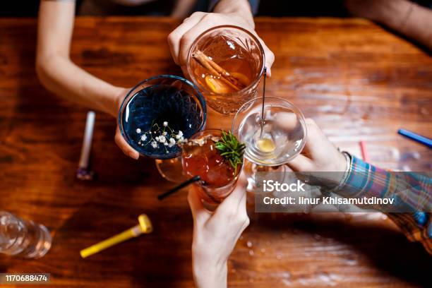 Friends Clinking By Glasses With Various Alcoholic Cocktails At Table Stock Photo - Download Image Now