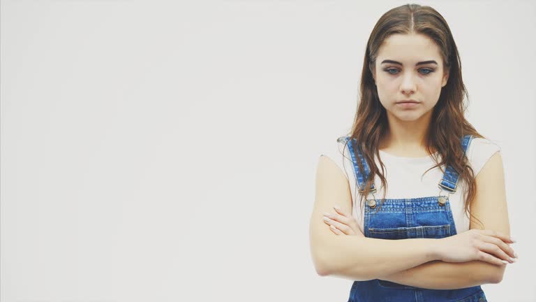 Lovely young female with long wavy hair is looking down to the side then looking at the camera with big blue eyes and raising her eyebrows. Her arms are folded.
