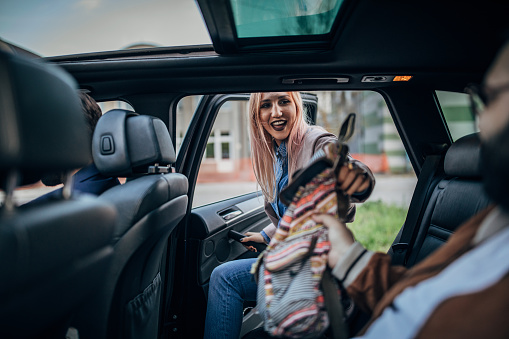 Young woman entering the car to share a ride with friends