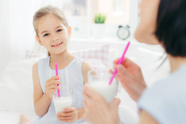 istock Pretty cute small child drinks delicious cocktail, has pleasant talk with her affectionate mother, enjoy together good morning, plan what to do during day off. Light tones. Spacious cozy bedroom 1170692510