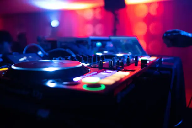 closeup of a dj mixer and controller with lights in the background in the night