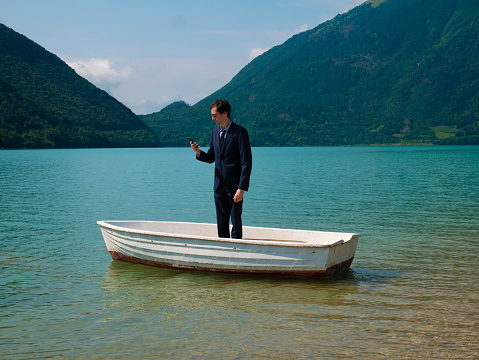 Man in suit on a small boat, looking at the smartphone.