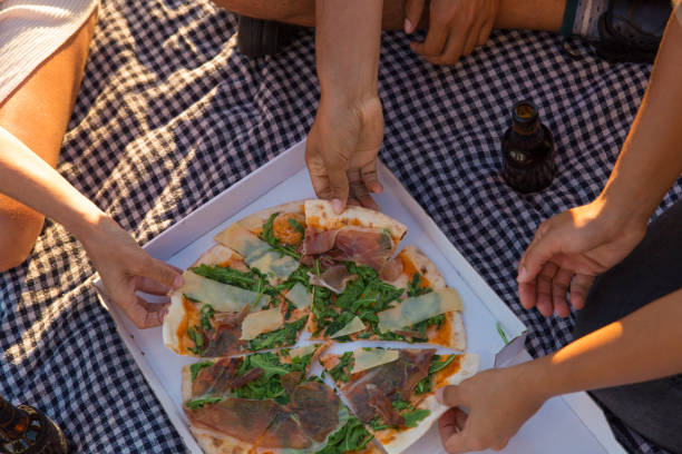 Top view of pizza in box and bottles of beer on picnic blanket