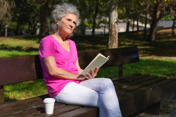 istock Serious focused old lady reading novel in park 1170700101