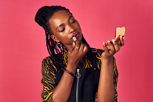 Studio shot of an attractive young woman applying lipstick while looking into a compact mirror
