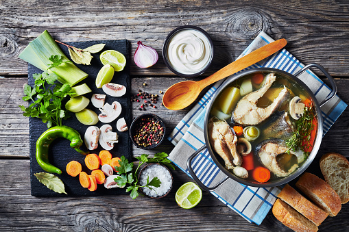 hot spicy Trout fish soup with vegetables and mushrooms in a saucepan on a wooden rustic table with ingredients, horizontal view from above, close-up, flat-lay