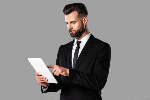 istock handsome businessman in black suit using digital tablet isolated on grey 1170710692