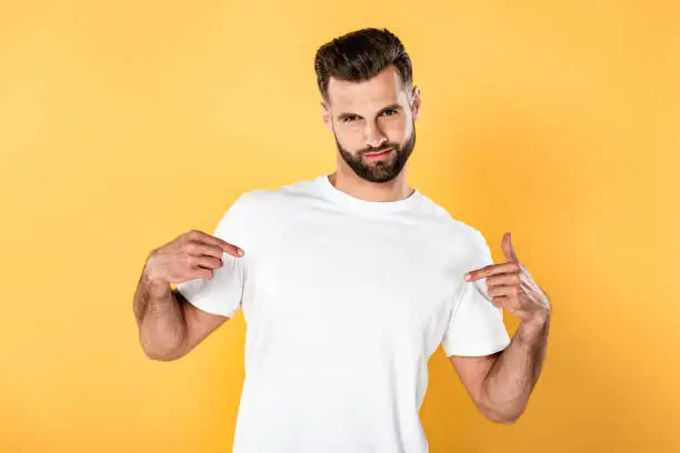 egotistical handsome man in white t-shirt pointing with fingers at himself isolated on yellow