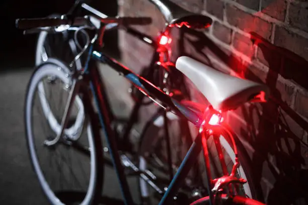 two bycicles at night with lights standing on a brick wall