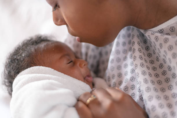 A newborn and mother in a hospital A young mother is kissing her newborn son on the forehead. They are at the hospital. The mother is wearing a hospital gown and the baby is wrapped tightly  in a white blanket. legacy concept photos stock pictures, royalty-free photos & images