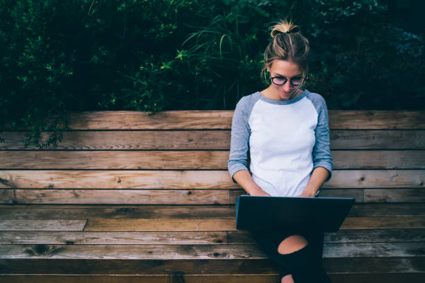 istock Hipster girl enjoying doing remote job outdoors using laptop computer and internet connection in town,young female using netbook for chatting and posting in social networks sitting on bench in city 1170720213