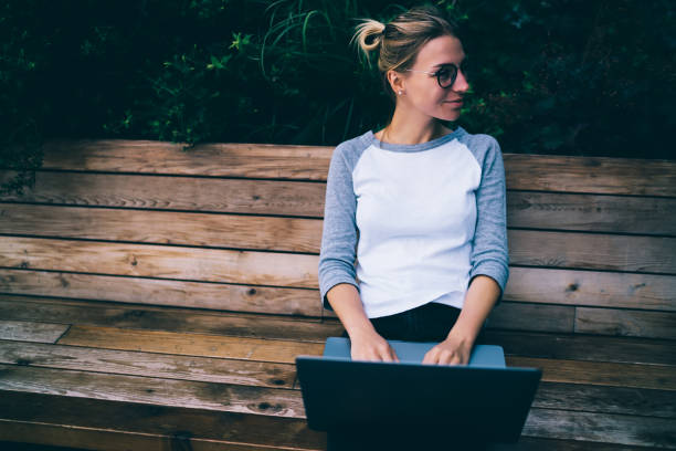 istock Smiling female freelancer typing publication on netbook satisfied with working sitting on bench in town,positive hipster girl share multimedia via laptop computer blogging while resting outdoors 1170720238