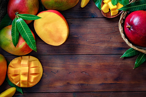 Healthy eating themes. Tropical Fruits: Basket with mangos making a frame with copy space in rustic kitchen