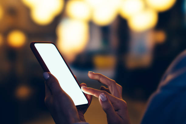 istock Women's hands hold mobile phone with   big copy space touch screen outdoors with evening bokeh light of city on background. Close up view of female person using smartphone with blank advertise display 1170728961