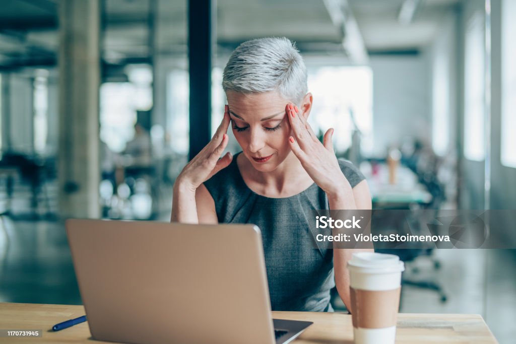 Empresaria con dolor de cabeza sentada en el escritorio - Foto de stock de Una sola mujer libre de derechos