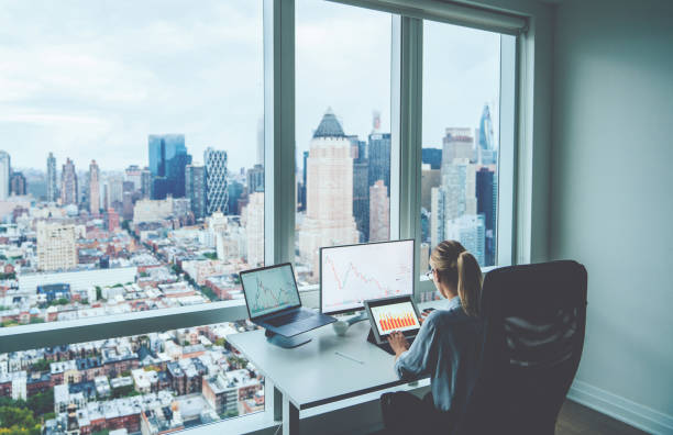 istock Rear view female employee working on PC computers with financial information on screen sitting at office table with downtown skyscrapers view behind window. Successful businesswoman at her workspace 1170740953