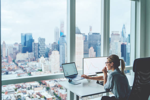 istock Back view of business woman sitting at panoramic skyscraper office desktop front PC computer with financial graphs and statistics on monitor. Analysis of digital market and investment in block chain 1170740965