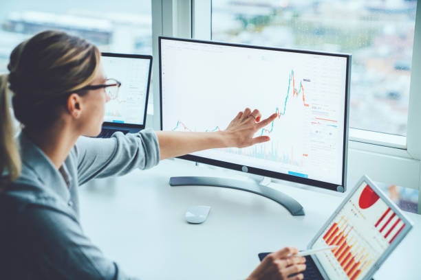 ビジネスウーマンは、可能なリスクと利益を計算するために金融市場を研究します。デスクトップでコンピュータの画面上を指す統計グラフを持つ女性エコノミスト会計のお金。為替に関す� - リスク 写真 ストックフォトと画像