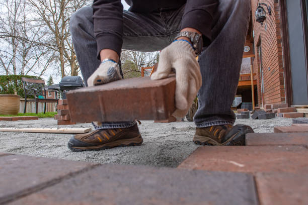 istock Installing paver bricks for patio in backyard. A workman's gloved hands use a hammer to place stone pavers. 1170742269