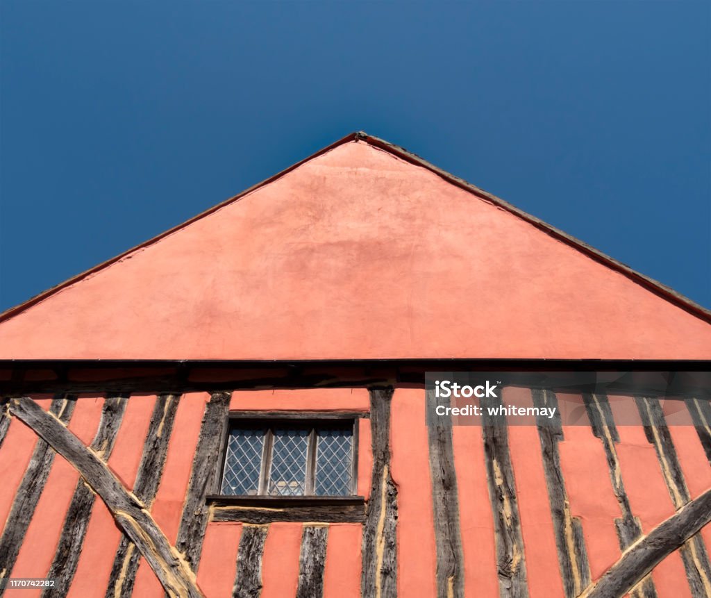 Part of a half-timbered building in Lavenham, Suffolk Part of the gable end of an ancient salmon-pink half-timbered building in Lavenham, Suffolk, Eastern England, on a bright sunny day with blue sky. Lavenham Stock Photo