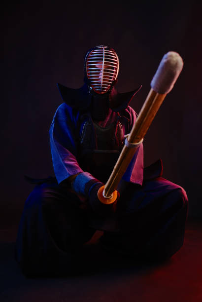istock Close up. Kendo fighter wearing in an armor, traditional kimono, helmet, sitting, practicing martial art with shinai bamboo sword, black background 1170742379