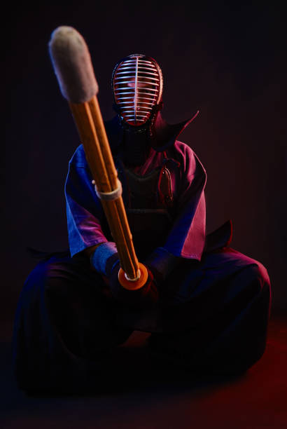 istock Close up. Kendo fighter wearing in an armor, traditional kimono, helmet, sitting, practicing martial art with shinai bamboo sword, black background 1170742449