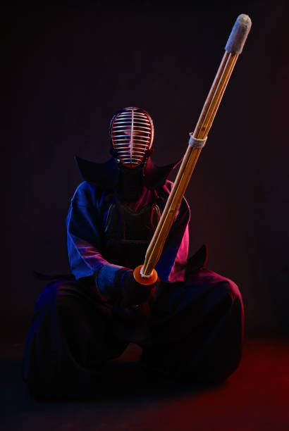 istock Close up. Kendo fighter wearing in an armor, traditional kimono, helmet, sitting, practicing martial art with shinai bamboo sword, black background 1170742514