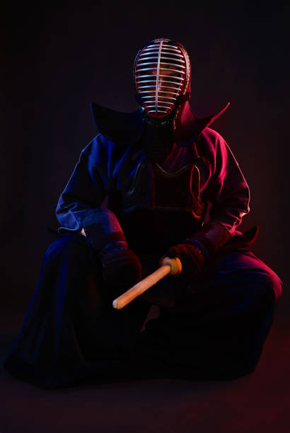 istock Close up. Kendo fighter wearing in an armor, traditional kimono, helmet, sitting, practicing martial art with shinai bamboo sword, black background 1170742591