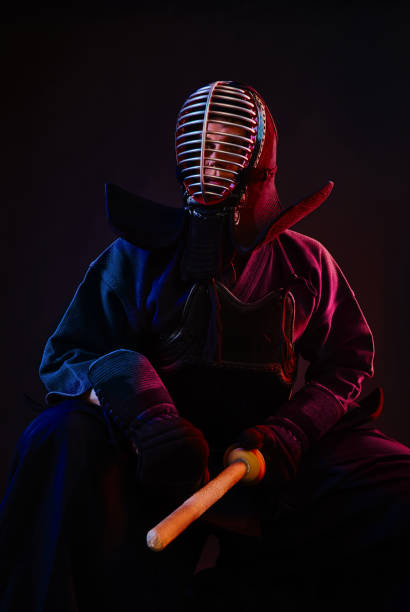 istock Close up. Kendo fighter wearing in an armor, traditional kimono, helmet, sitting, practicing martial art with shinai bamboo sword, black background 1170742683