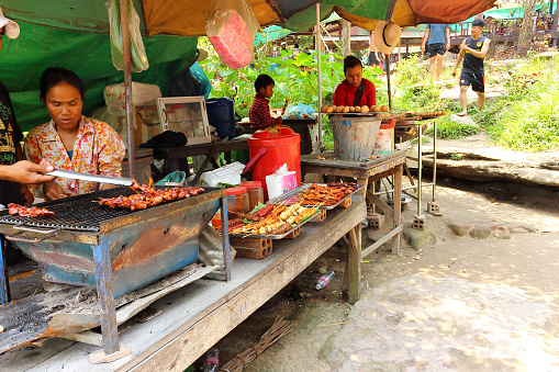Siem Reap, Cambodia- Mart 25, 2018: Unhurried cambodian life. Cooking local cuisine on grill and barbecue for tourists on the counter and travelers of a street food vendor in Cambodia.